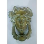 A late 19th/early 20th century brass door knocker in the form of a classical female head and foliate