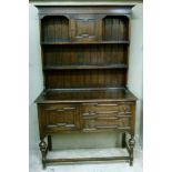 An oak dresser with flared cornice the shelved back with geometric panelled cupboard to the top