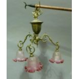 A brass electrolier of three scrolled arms with opaque and cranberry tinted light shades with folded