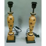 A pair of turned wooden table lamps decorated with fleur de lys on square bases with ebonised