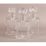 A SET OF THREE HEAVY CUT GLASS DECANTERS of canted square form with disc tops and heavy cut