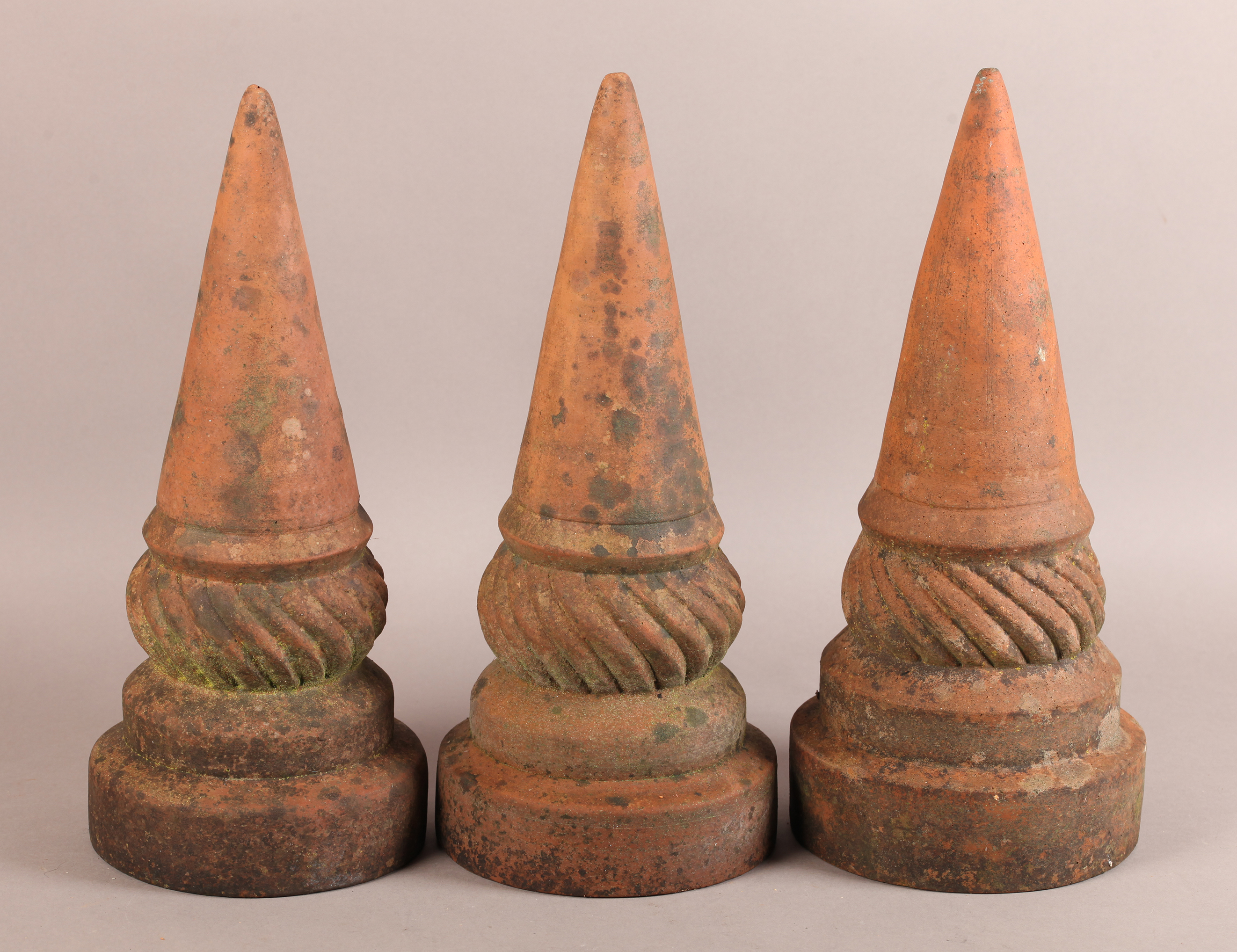 A SET OF THREE 19TH CENTURY TERRACOTTA FINIALS of conical and writhen form on circular plinth