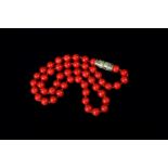 A CORAL NECKLACE of spherical 10mm beads, interspaced with small gold beads, fastened with barrel