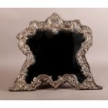 AN EDWARD VII DRESSING TABLE MIRROR of shield shape with strut, the design of rocaille, leaf curls