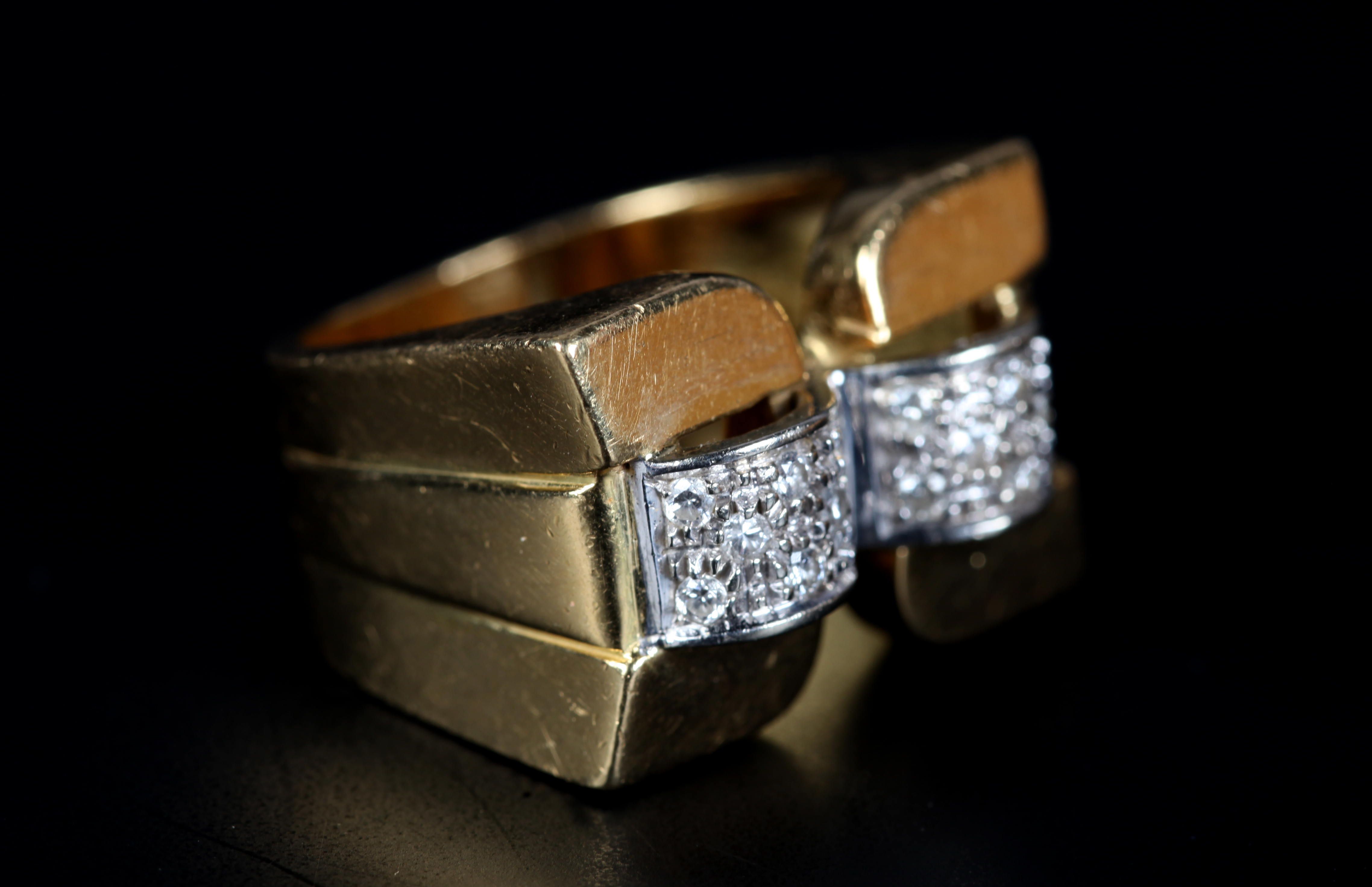 AN ART DECO STYLE DIAMOND RING the brilliant cut stone grain set to two domed square strips of white