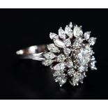 A DIAMOND CLUSTER RING claw set to the centre with a brilliant cut stone raised against a tiered
