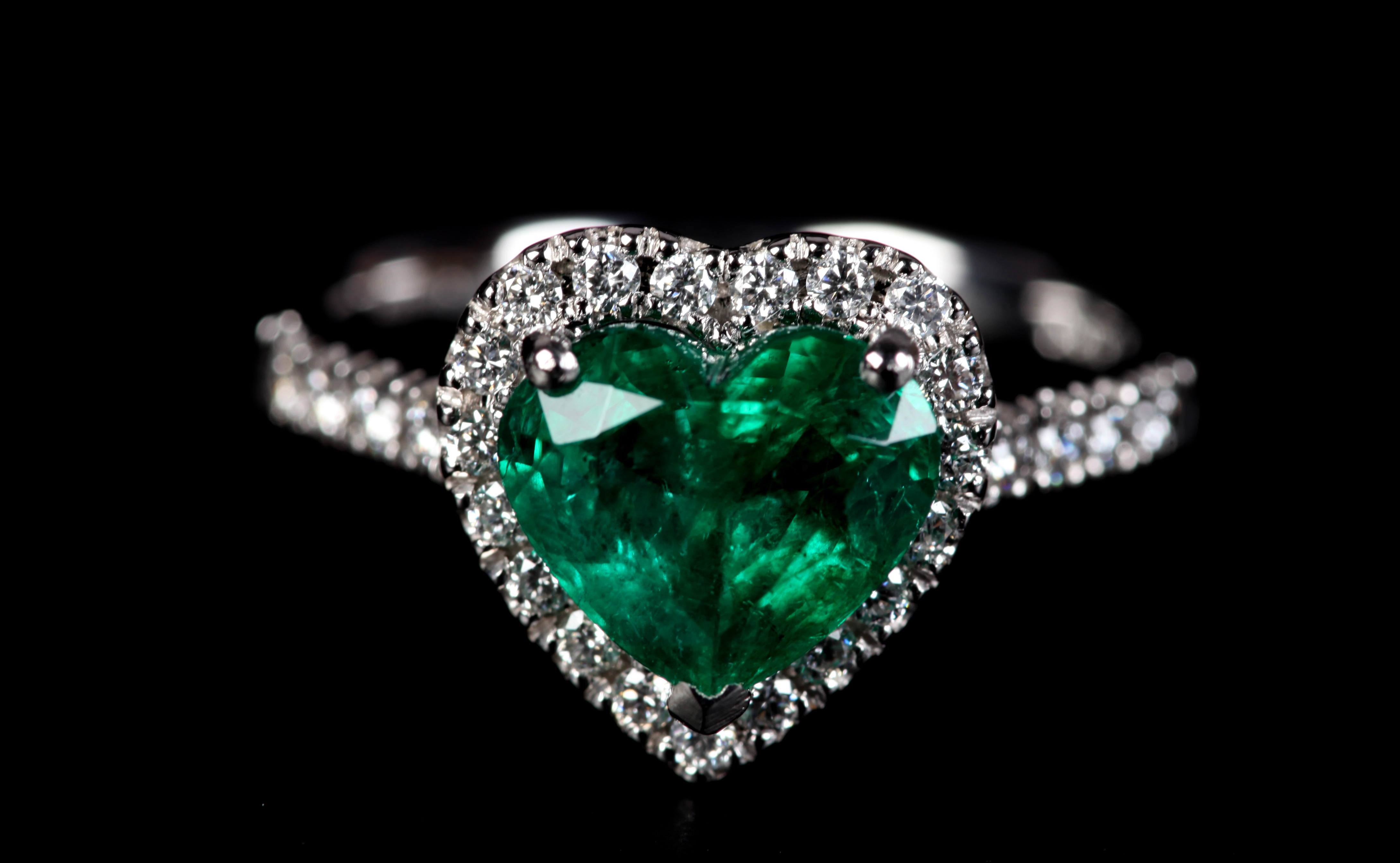 AN EMERALD AND DIAMOND CLUSTER RING in platinum the heart shaped faceted emerald claw set, raised