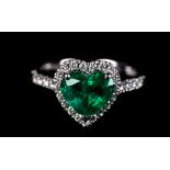 AN EMERALD AND DIAMOND CLUSTER RING in platinum the heart shaped faceted emerald claw set, raised