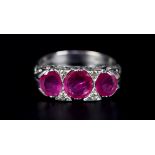 A RUBY AND DIAMOND RING in 18ct white gold the three graduated oval faceted rubies claw set inline