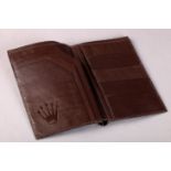 A ROLEX WALLET in brown leather, coronet embossed to the interior with leaves for cards and notes,