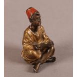 AN AUSTRIAN COLD CAST AND PAINTED BRONZE FIGURE modelled as a young boy, seated with his legs