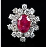 A RUBY AND DIAMOND CLUSTER RING claw set to the centre with an oval faceted ruby raised against a