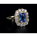 A SAPPHIRE AND DIAMOND CLUSTER RING in 18ct gold, the step cut sapphire collet set within a surround