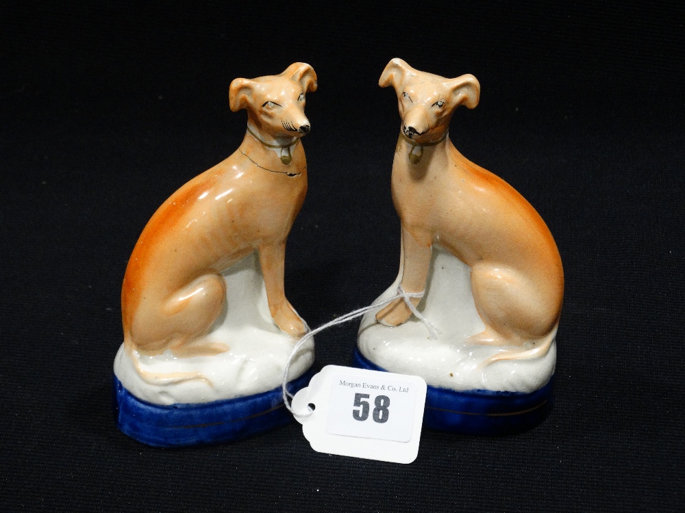 A Pair Of Staffordshire Pottery Seated Greyhounds On Blue Lined Cushions (1 AF)