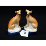 A Pair Of Staffordshire Pottery Seated Greyhounds On Blue Lined Cushions (1 AF)