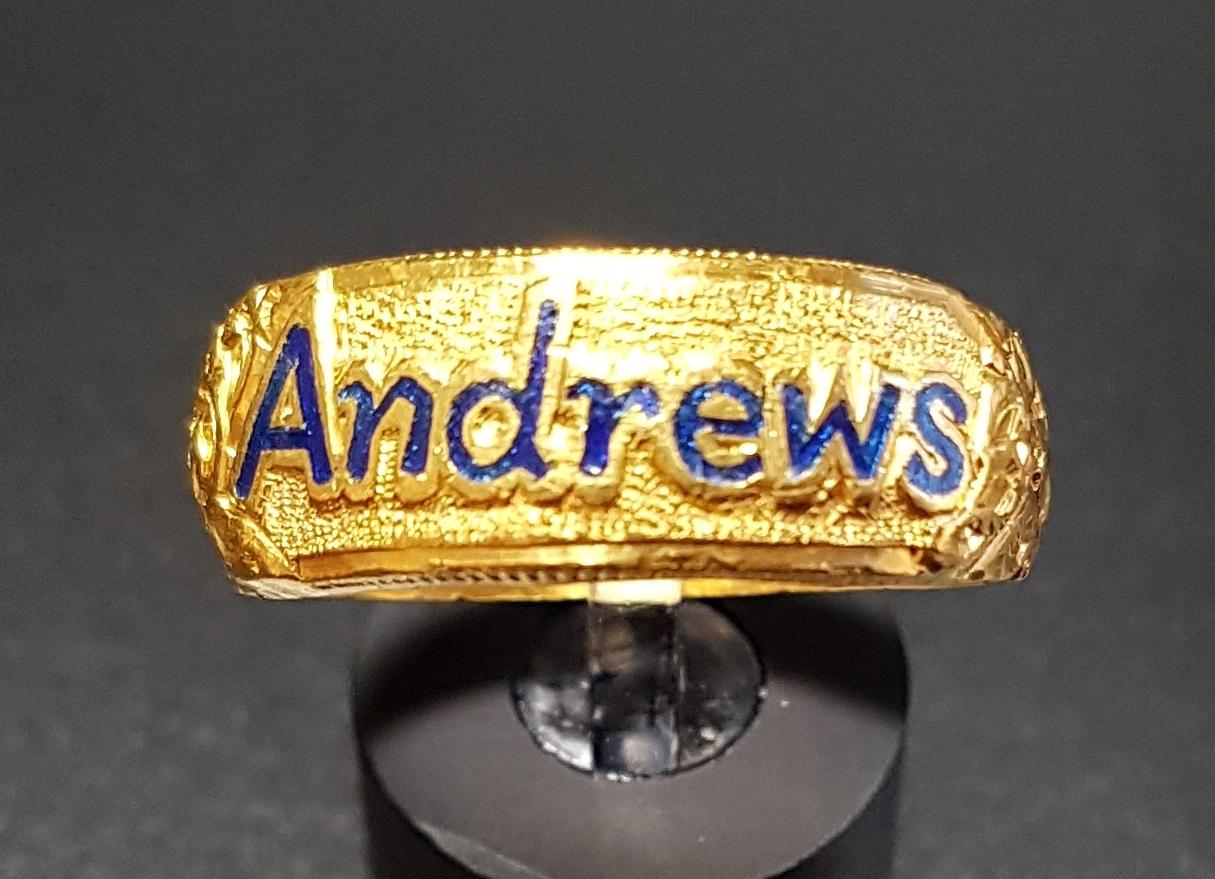 TWENTY-THREE CARAT GOLD DRESS RING with enamelled 'Andrews' flanked by motif and scroll decorated