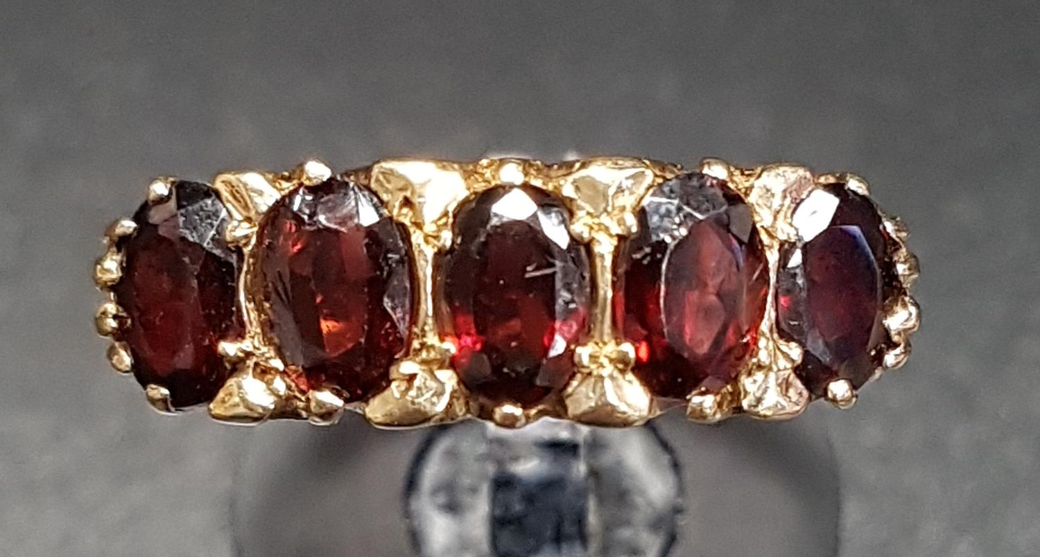 GARNET FIVE STONE RING the five oval cut garnets on nine carat gold shank with scroll decorated