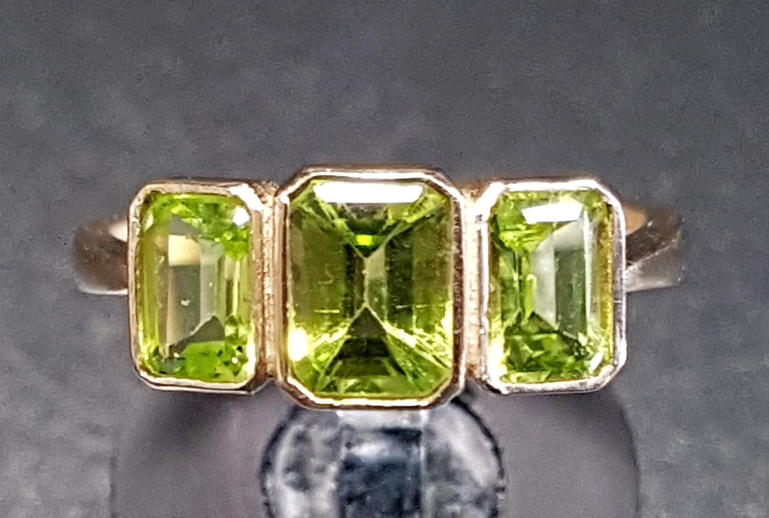 GRADUATED PERIDOT THREE STONE RING the emerald cut peridots in bezel settings, on nine carat gold