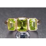 GRADUATED PERIDOT THREE STONE RING the emerald cut peridots in bezel settings, on nine carat gold