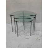 NEST OF GLASS TABLES of irregular form standing on tapering chrome supports, 46cm high