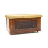 TEAK BLANKET BOX with a lift up stuffover lid above a carved front panel, standing on later castors,