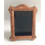 EDWARDIAN STYLE COPPER PHOTOGRAPH FRAME the shaped frame with relief floral decoration, on easel