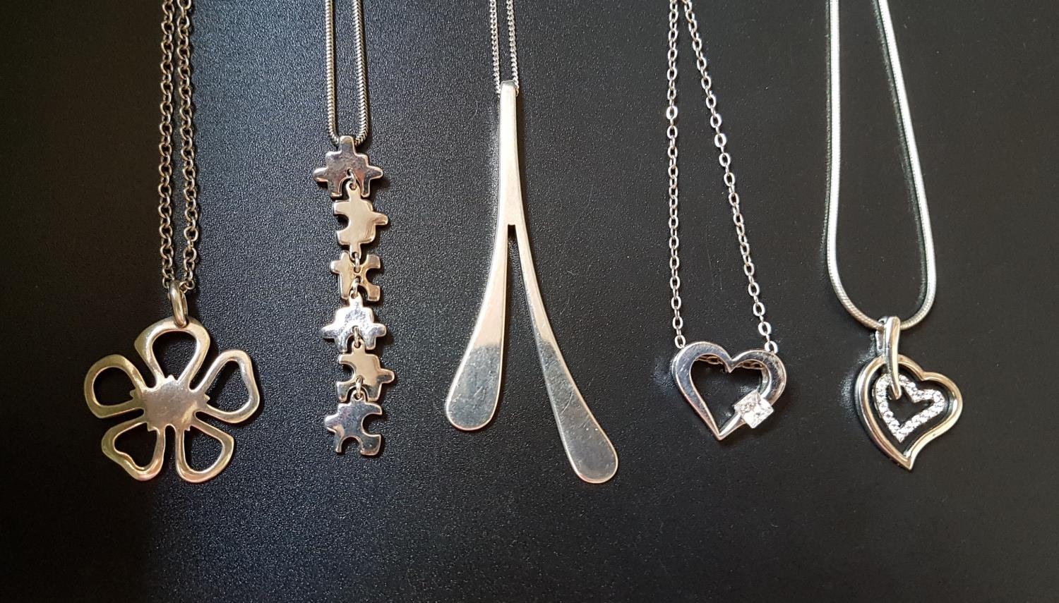 FIVE SILVER PENDANTS ON SILVER CHAINS comprising one with jigsaw style links, two CZ set heart