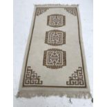 WOOL RUG with a cream ground and three geometric motifs encased by a cream and brown border,