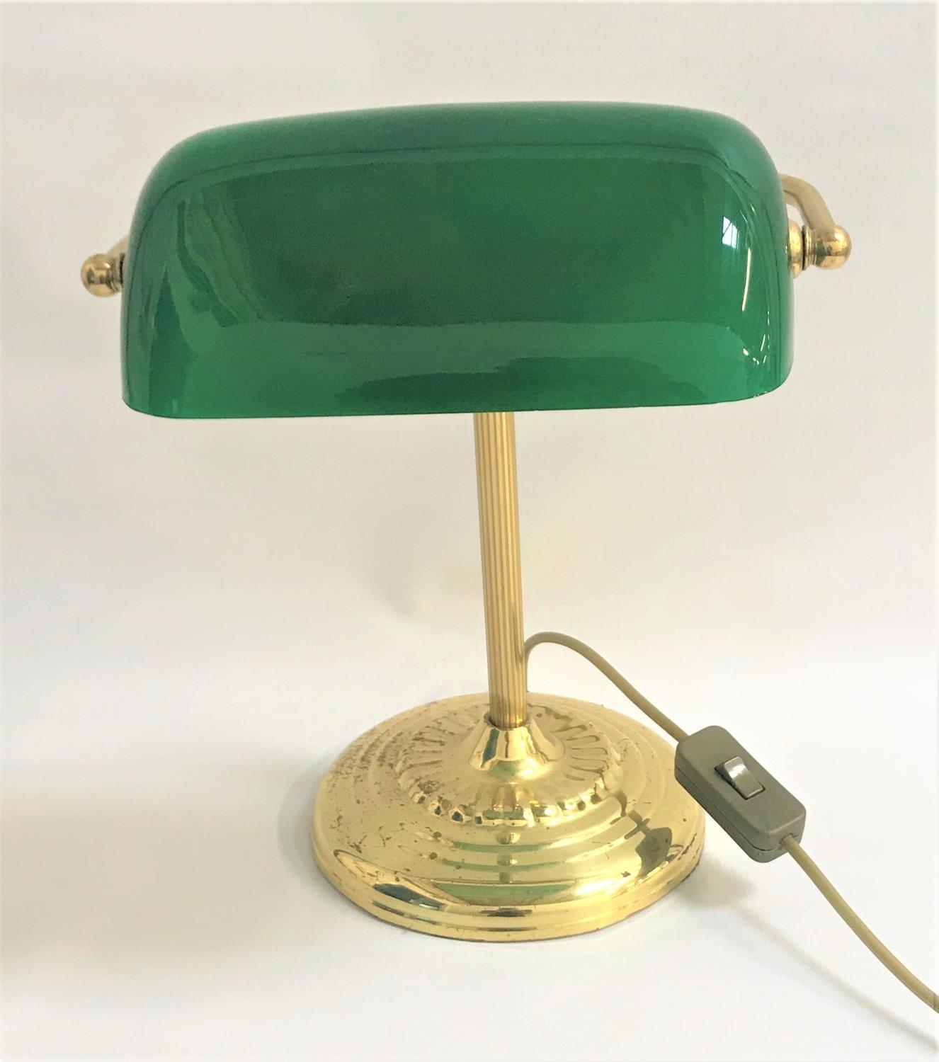 BRASS DESK LAMP raised on a circular stepped base with a tubular column and green glass shade,