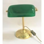 BRASS DESK LAMP raised on a circular stepped base with a tubular column and green glass shade,