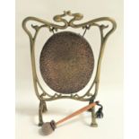 ART NOUVEAU BRASS TABLE GONG of shaped outline with an oval hammered gong, and a suede covered