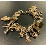 SILVER CHARM BRACELET with a variety of mostly silver charms, including a heart padlock, bagpipes,