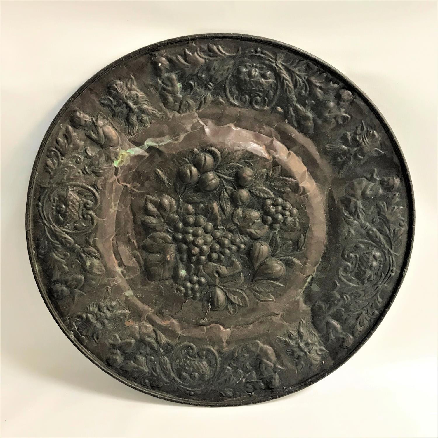 EMBOSSED BRASS CHARGER decorated with face masks, cherubs and scrolls around a central cartouche