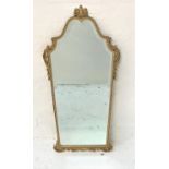 METAL GILT WALL MIRROR with an arched shaped bevelled plate, the frame surmounted with a stylised