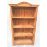 NATURAL PINE BOOKCASE with a shaped top above four shelves flanked by carved columns, standing on