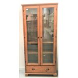 WAXED PINE DISPLAY CABINET the moulded top above a pair of glazed doors opening to reveal adjustable
