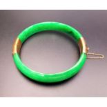 FOURTEEN CARAT GOLD MOUNTED HINGED JADE BANGLE the gold mounts with textured detail, with safety