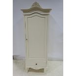 A WHITE PAINTED WARDROBE the shaped cornice above a panel door containing hanging rail and shelves