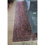 A WOOL RUNNER the red ground with central floral panel within a conforming border 265cm x 75cm