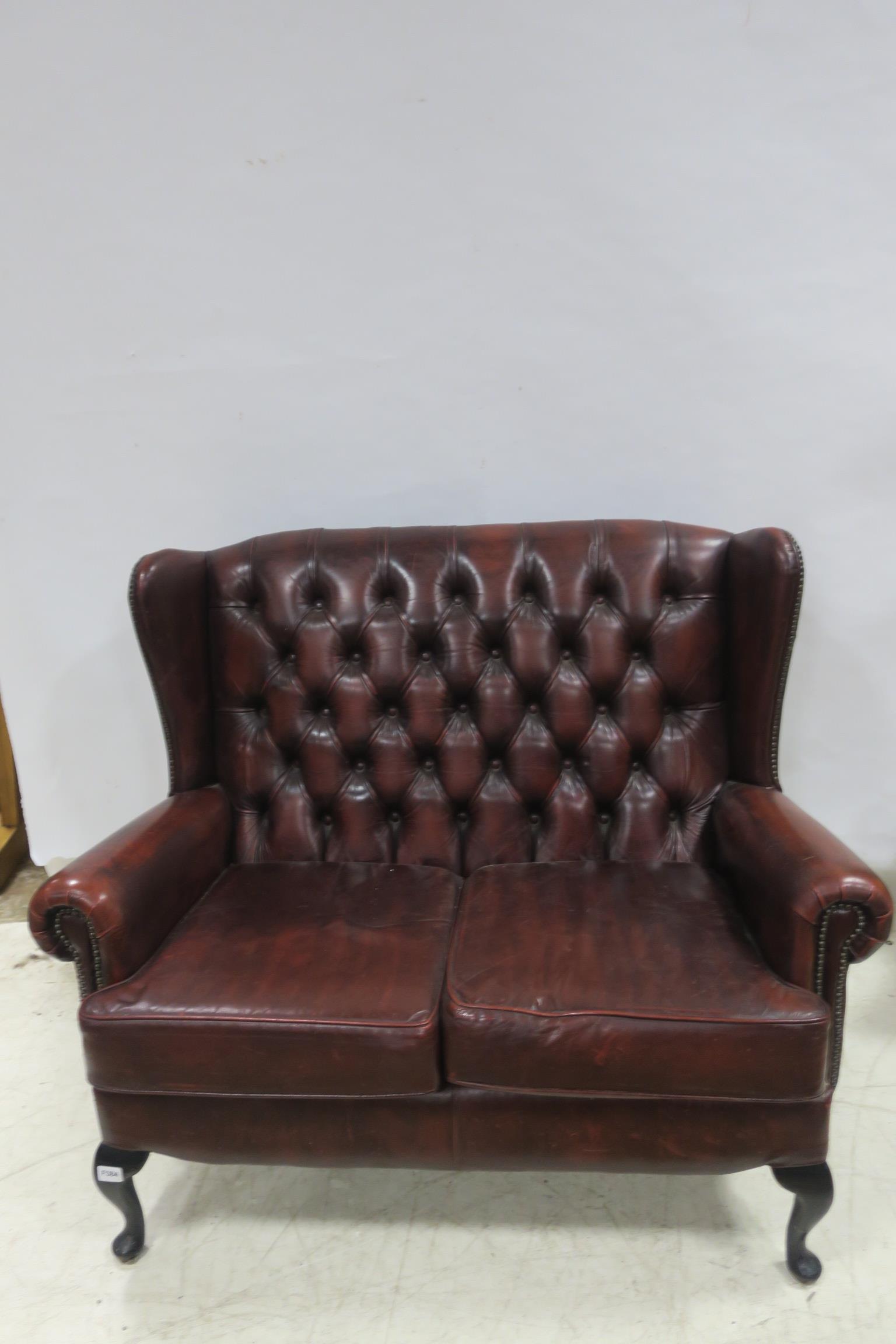 A RED HIDE UPHOLSTERED TWO SEATER WINGED BACK SETTEE with deep buttoned upholstered back and loose