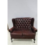 A RED HIDE UPHOLSTERED TWO SEATER WINGED BACK SETTEE with deep buttoned upholstered back and loose