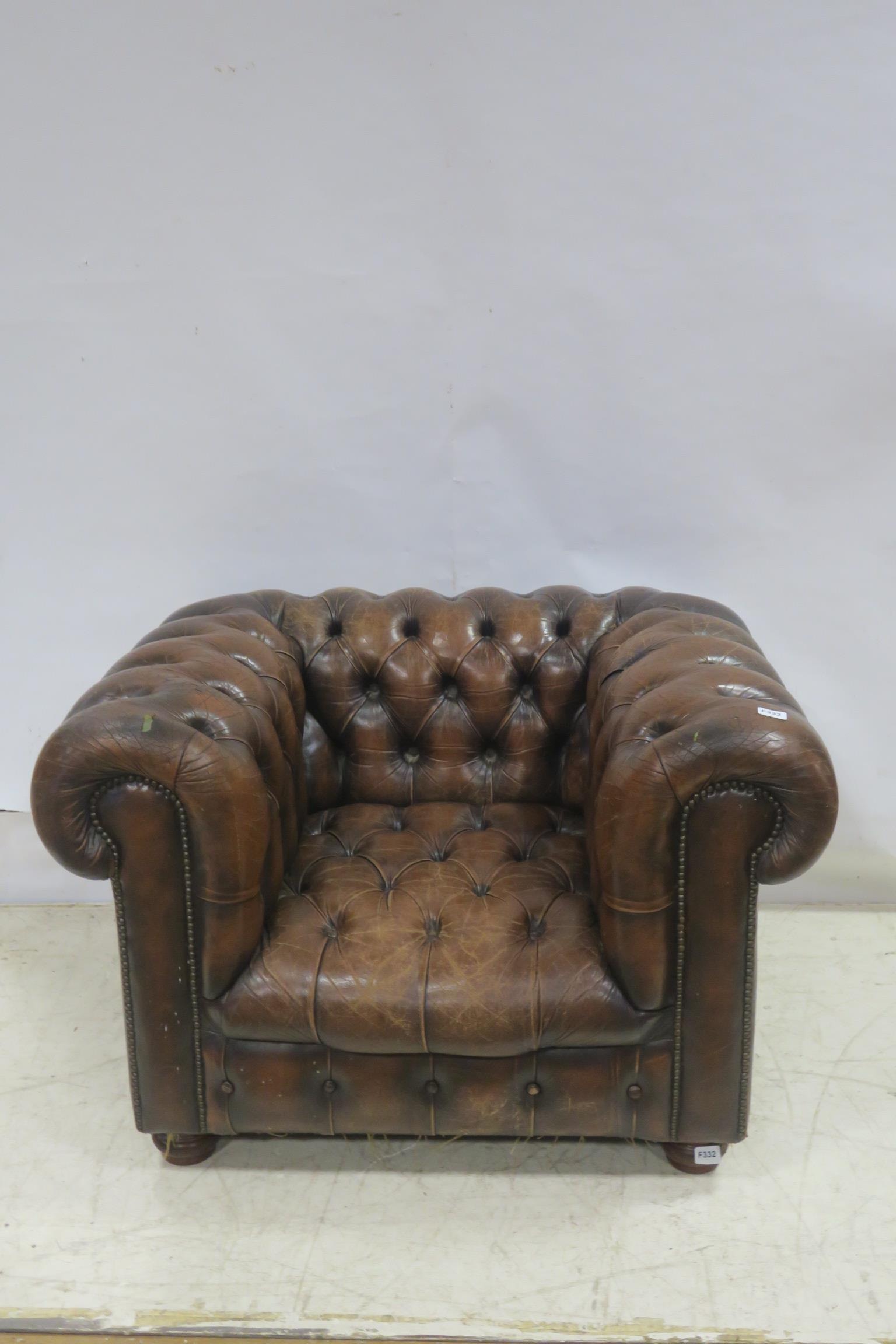 A HIDE UPHOLSTERED AND BUTTONED LIBRARY ARMCHAIR with scroll over back and arms on bun feet