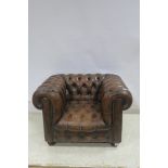 A HIDE UPHOLSTERED AND BUTTONED LIBRARY ARMCHAIR with scroll over back and arms on bun feet