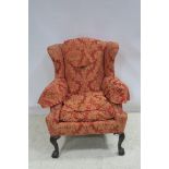 A CHIPPENDALE DESIGN MAHOGANY AND UPHOLSTERED WING CHAIR with scroll over arms and loose cushion on