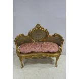 A CONTINENTAL GILTWOOD AND BERGERE SETTEE with foliate carved top rail and loose cushion on