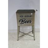 A WHITE METAL CONTAINER raised on tapering legs with carrying handles inscribed Ice Cold Beer 83cm