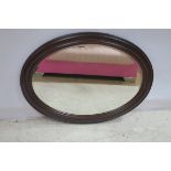 A STAINED WOOD MIRROR with oval bevelled glass plate within a moulded frame 100cm x 76cm