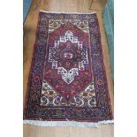 AN ORIENTAL WOOL RUG the wine ground with central panel filled with palmets hooks and lozenges