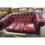 A RED HIDE UPHOLSTERED BUTTON BACK LIBRARY SETTEE with scroll over back and arms and loose cushions