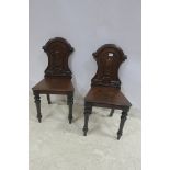 A PAIR OF 19TH CENTURY MAHOGANY HALL CHAIRS each with a shaped back and carved plaque above a